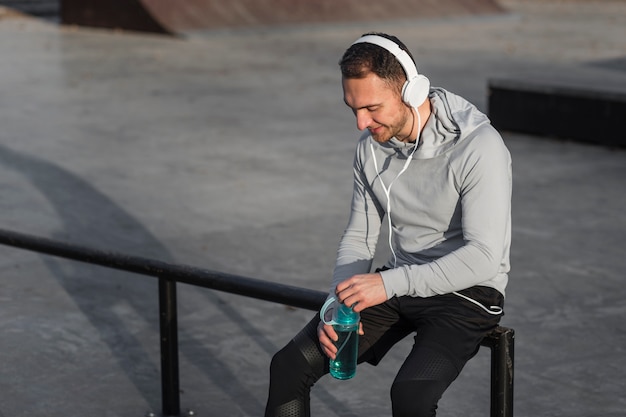 Hörende Musik des athletischen Mannes und Halten einer Flasche Wassers