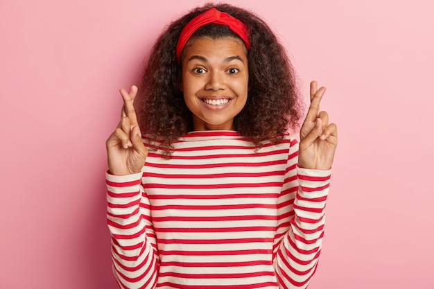 hoffnungsvolles Mädchen mit dem lockigen Haar, das im gestreiften roten Pullover aufwirft