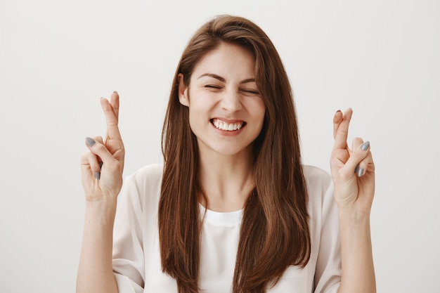 Hoffnungsvolles positives Mädchen kreuzen die Finger, während sie Wunsch machen, optimistisch lächelnd