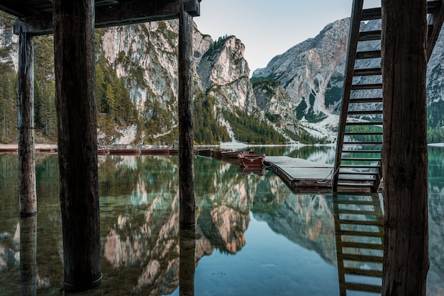 Kostenloses Foto hohe felsige berge spiegelten sich im braies-see mit holztreppen nahe dem pier in italien wider