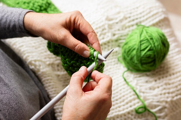 Hohe Sicht auf eine Person, die mit grünem Faden strickt