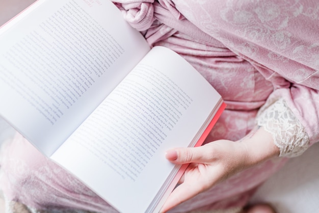 Hohe Winkelansicht einer Frau, die ein rosa Kleid trägt, das ein englisches Buch liest