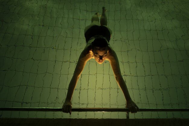 Hohe Winkelansicht einer Frau, die in einem Pool unter den Lichtern schwimmt - perfekt für Sportkonzepte