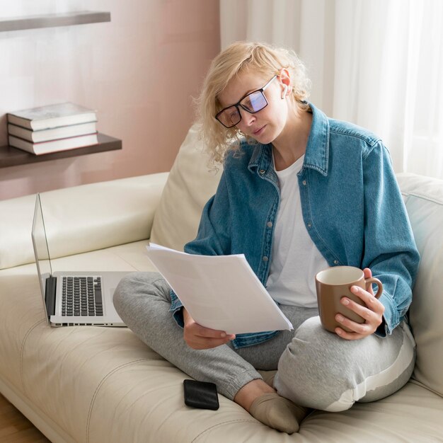 Hohe Winkelfrau, die auf Couch arbeitet und Kaffee trinkt