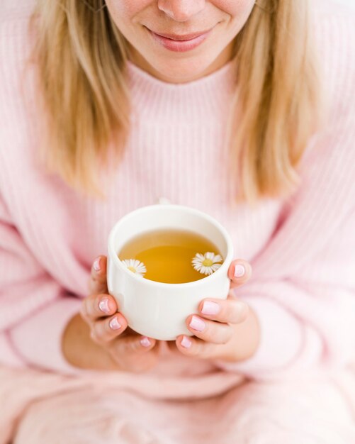 Hohe Winkelfrau, die weiße Tasse mit Tee und Blumen hält