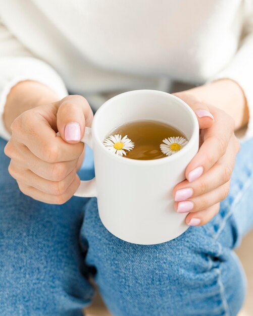 Hohe Winkelfrau, die weißen Becher mit Tee und Blumen hält