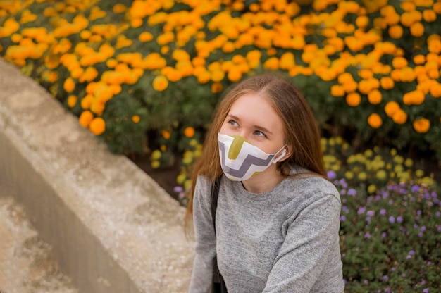 Hohe Winkelfrau mit medizinischer Maske, die neben einem Garten sitzt