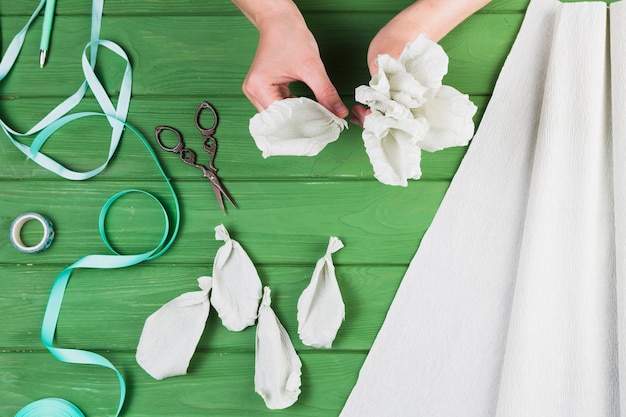 Hohe Winkelsicht der Frau gefälschte weiße Blume mit Scissor und Band über Tabelle vorbereitend