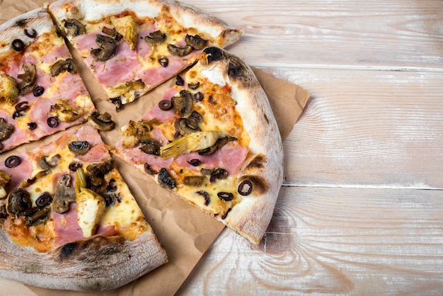 Hohe Winkelsicht der geschnittenen Pilzpfefferonipizza auf braunem Papier über Holztisch