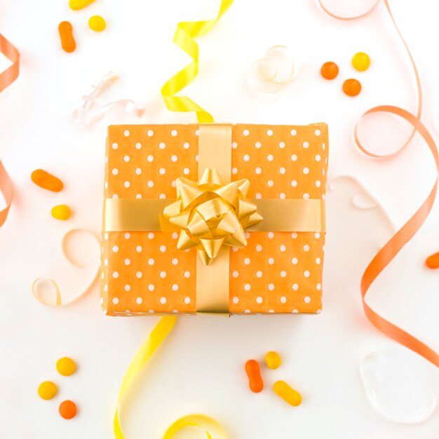 Hohe Winkelsicht des Geburtstagsgeschenks mit Bändern und Süßigkeiten auf weißer Oberfläche