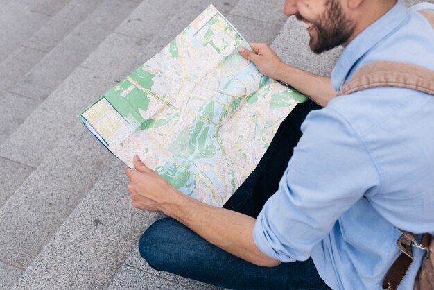 Hohe Winkelsicht des lächelnden Mannes sitzend auf Treppenhaus und Karte lesend