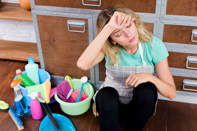 Kostenloses Foto hohe winkelsicht einer überarbeiteten reinigungsfrau, die auf boden mit reinigungswerkzeugen und -produkten sitzt