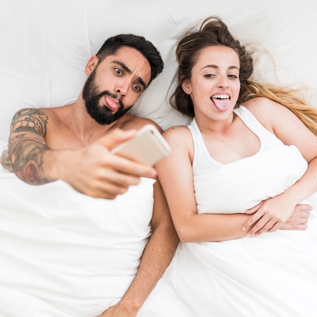 Hohe Winkelsicht eines Paares, das heraus Zunge beim Nehmen von selfie auf Smartphone haftet