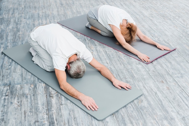 Hohe winkelsicht eines paares in der weißen ausstattung, die yoga-positionen ausdehnend übt