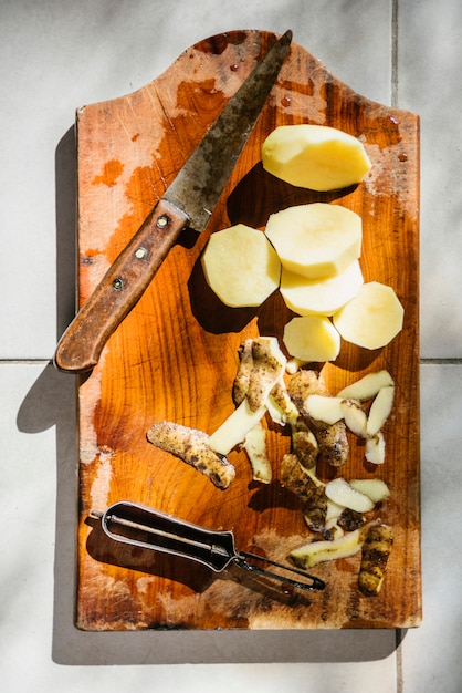 Hohe Winkelsicht von geschnittenen Kartoffeln mit Messer auf hölzernem Schneidebrett