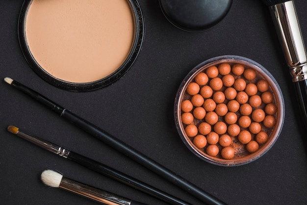 Kostenloses Foto hohe winkelsicht von kosmetischen produkten mit make-upbürste auf schwarzem hintergrund
