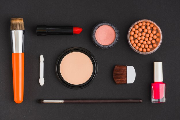 Hohe Winkelsicht von verschiedenen kosmetischen Produkten und von Make-upbürste auf schwarzem Hintergrund
