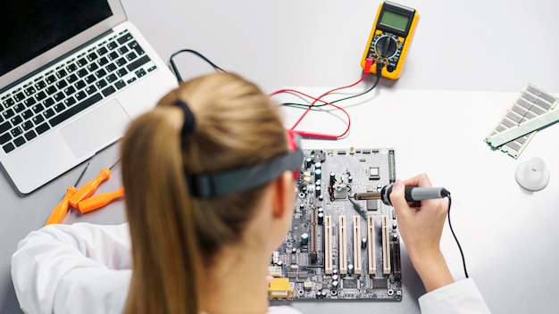 Hoher Winkel der Technikerin mit Lötkolben und Elektronik-Motherboard