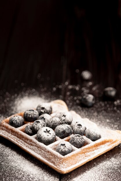 Hoher Winkel der Waffel mit den Blaubeeren bedeckt im Puderzucker