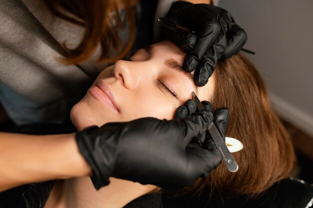 Hoher Winkel der weiblichen Kosmetikerin, die eine Augenbrauenbehandlung für Frau tut
