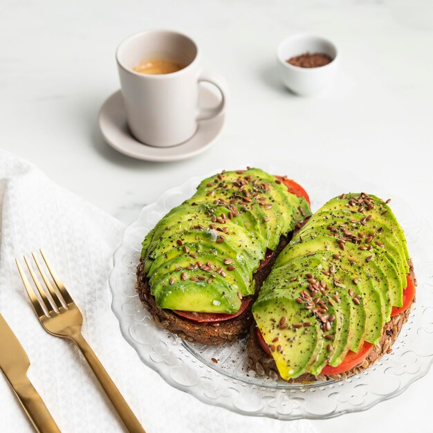 Hoher Winkel des Avocado-Toasts auf Teller mit Besteck und Kaffee