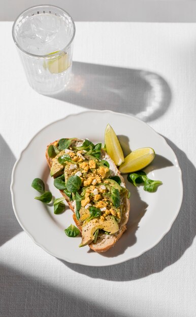 Hoher Winkel des Avocado-Toasts auf Teller mit eisigem Glas Wasser