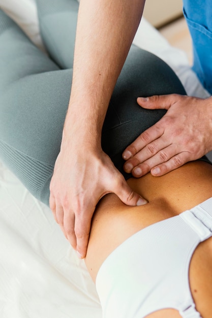Hoher Winkel des männlichen osteopathischen Therapeuten, der die untere Rückenwirbelsäule der Patientin überprüft