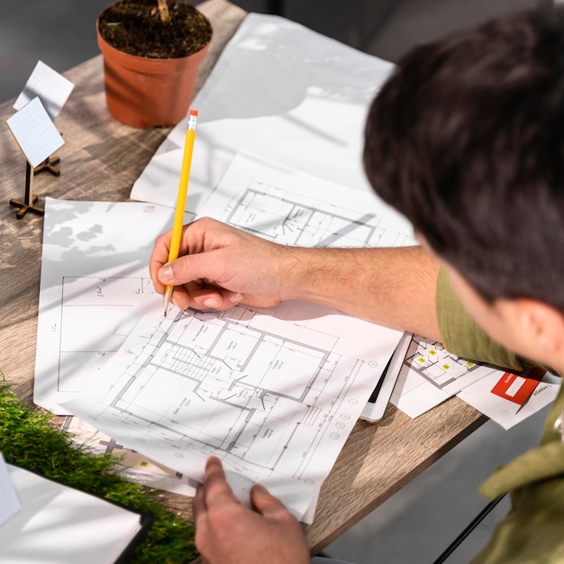 Hoher Winkel des Mannes, der an einem umweltfreundlichen Windkraftprojekt mit Papieren und Bleistift arbeitet