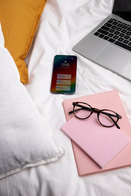 Hoher Winkel des Smartphones auf dem Bett mit Laptop und Brille