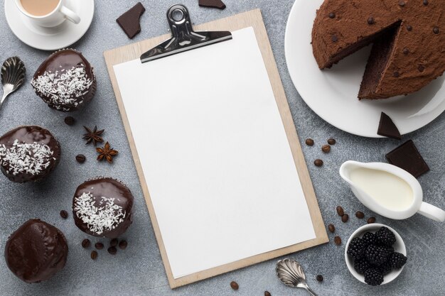 Hoher Winkel von Schokoladenkuchen mit Notizblock und anderen Desserts