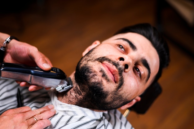 Hoher Winkelfriseur, der den Bart des Kunden rasiert