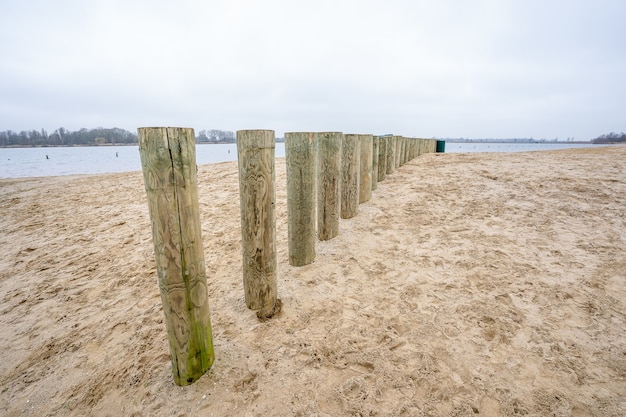 Hoher Winkelschuss der hölzernen Wellenbrecherstangen auf einem Strandsand