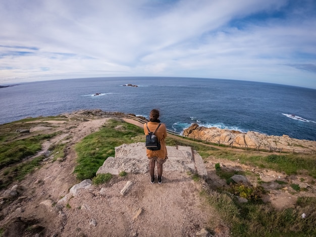 Hoher Winkelschuss einer stilvollen Frau, die steht und das ruhige Meer nahe Coruna, Spanien betrachtet