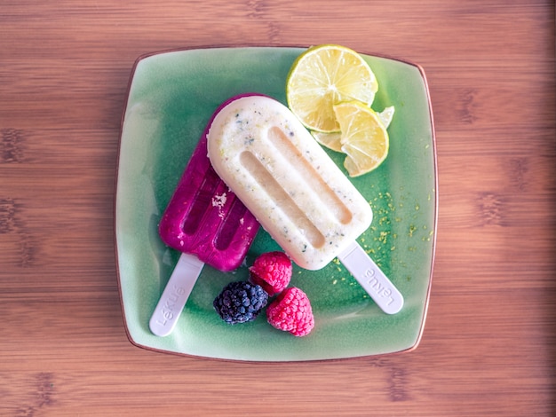 Hoher Winkelschuss von zwei köstlichen Eis am Stiel mit Früchten in einem grünen Teller auf einem Holztisch