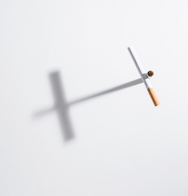 Hohes Winkelsichtkreuzzeichen gemacht von der Zigarette mit ihm Schatten an lokalisiert auf weißem Hintergrund