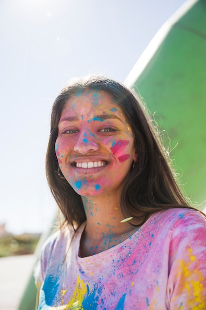 Holi-Farbpulver über dem lächelnden Gesicht der jungen Frau, das Kamera betrachtet