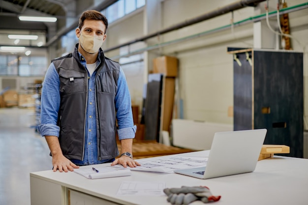 Holzbearbeitungsingenieur mit Gesichtsmaske, der in einer Industrieanlage arbeitet und in die Kamera blickt