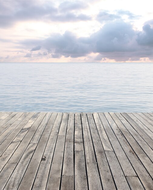 Holzboden und blaues Meer mit Wellen und bewölktem Himmel