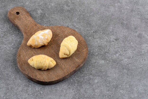 Holzbrett mit drei frischen Keksen auf Marmortisch.