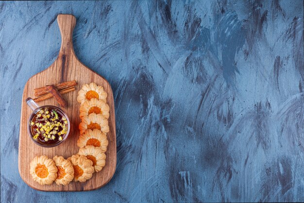 Holzbrett mit Geleeplätzchen und Tasse Tee auf blauem Hintergrund.