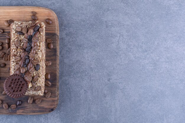 Holzbrett unter einem Stück Kuchen mit Keks und Kaffeebohnen auf Marmoroberfläche