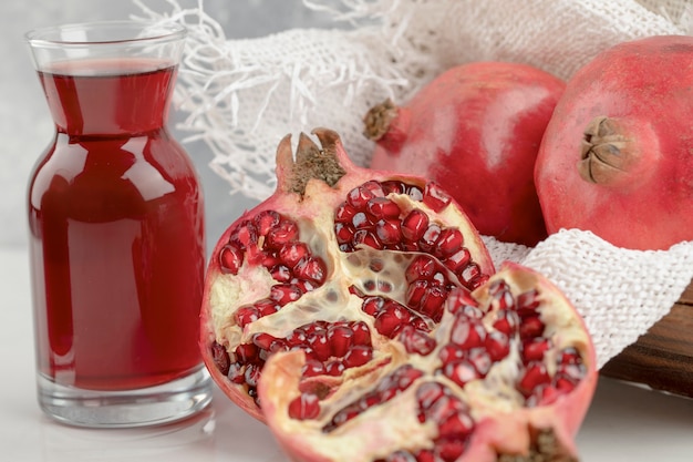 Holzkiste mit frischen roten Granatäpfeln und köstlichem Saft auf weißem Tisch.