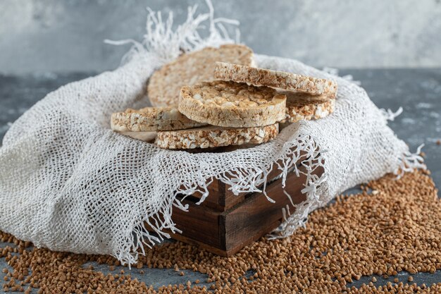 Holzkiste mit luftigem Knäckebrot und rohem Buchweizen auf Marmoroberfläche