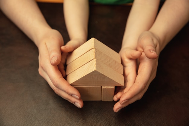 Holzkonstrukteur wie Haus sammeln. Nahaufnahme Schuss von Frauen- und Kinderhänden, die verschiedene Dinge zusammen tun. Familie, Zuhause, Bildung, Kindheit, Wohltätigkeitskonzept. Mutter und Sohn oder Tochter.