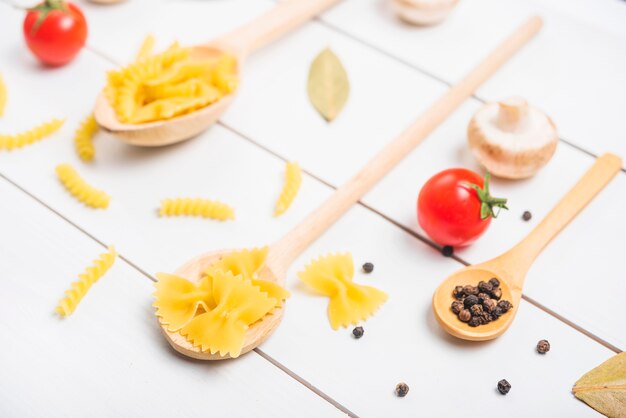 Holzlöffel mit Nudeln Fusilli; Farfalle und Pfefferkörner mit Tomaten; Pilz; Lorbeerblatt