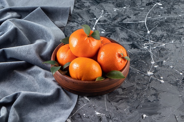 Holzschale mit frischen saftigen Orangen auf Marmoroberfläche.