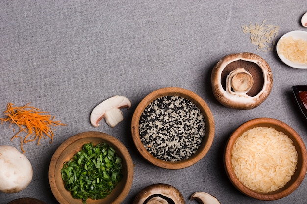 Holzschale Schnittlauch; Sesamsamen; Reiskörner; Pilz und geriebene Karotte auf grauem Leinentuch
