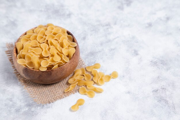 Holzschale voll roher trockener Farfalle-Nudeln auf Marmortisch. Hochwertiges Foto