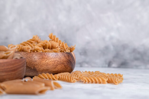 Holzschalen mit italienischen ungekochten trockenen Nudeln auf Steintisch. Hochwertiges Foto