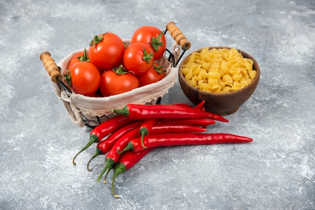 Holzschalen mit rohen Nudeln mit roten Chilischoten und Tomaten auf Marmor.